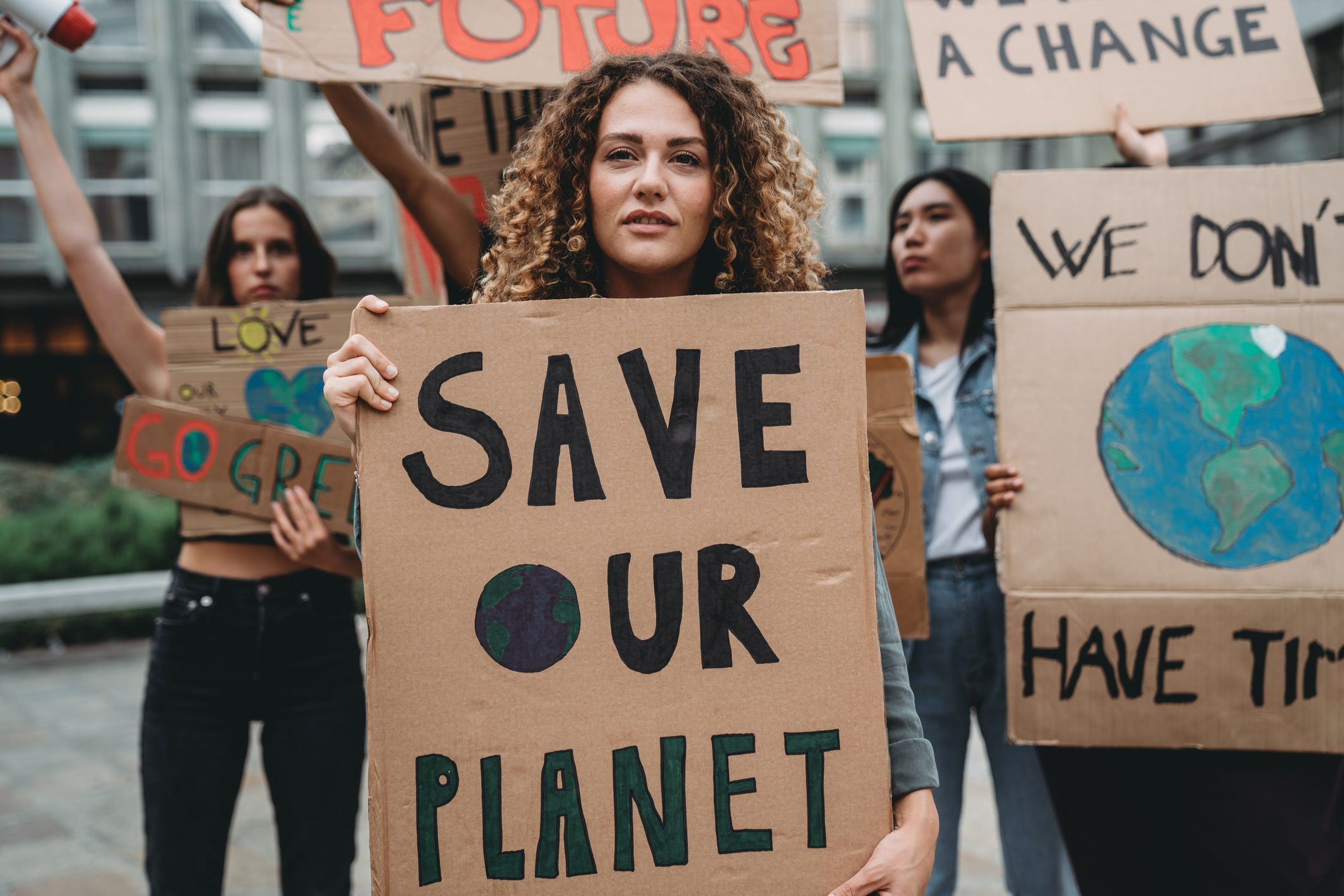A group of young adult people are marching together on strike against climate change. They are holding cardboard signs. Multi ethnic group of people. Portrait of a girl holding a sign with the text "save our planet" on it.
