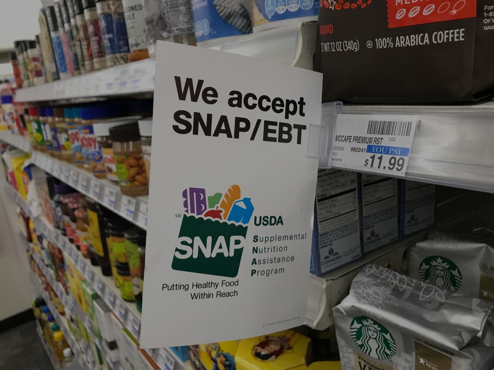 A close-up image of a flyer on a grocery aisle shelf that reads "We accept SNAP/EBT"