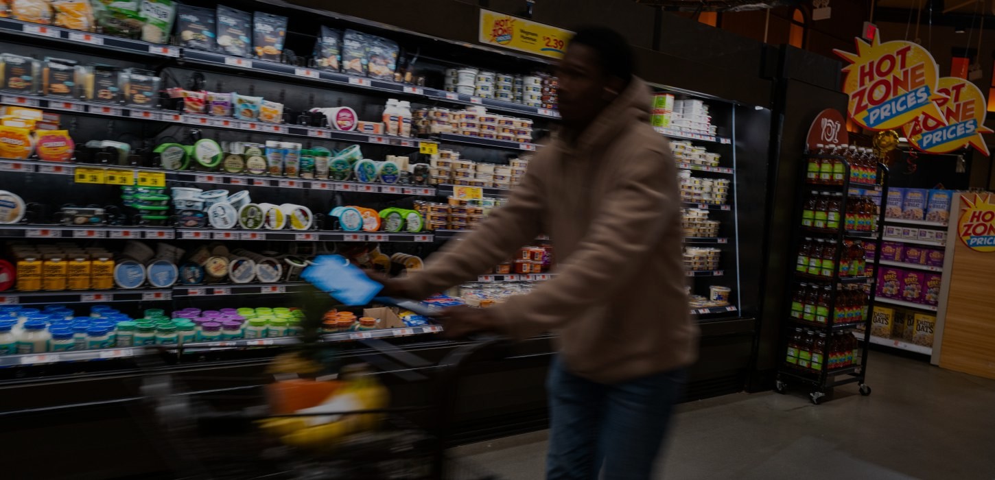 A blurred image of a shopper in a grocery store with signs that read "hot zone prices" in the background.