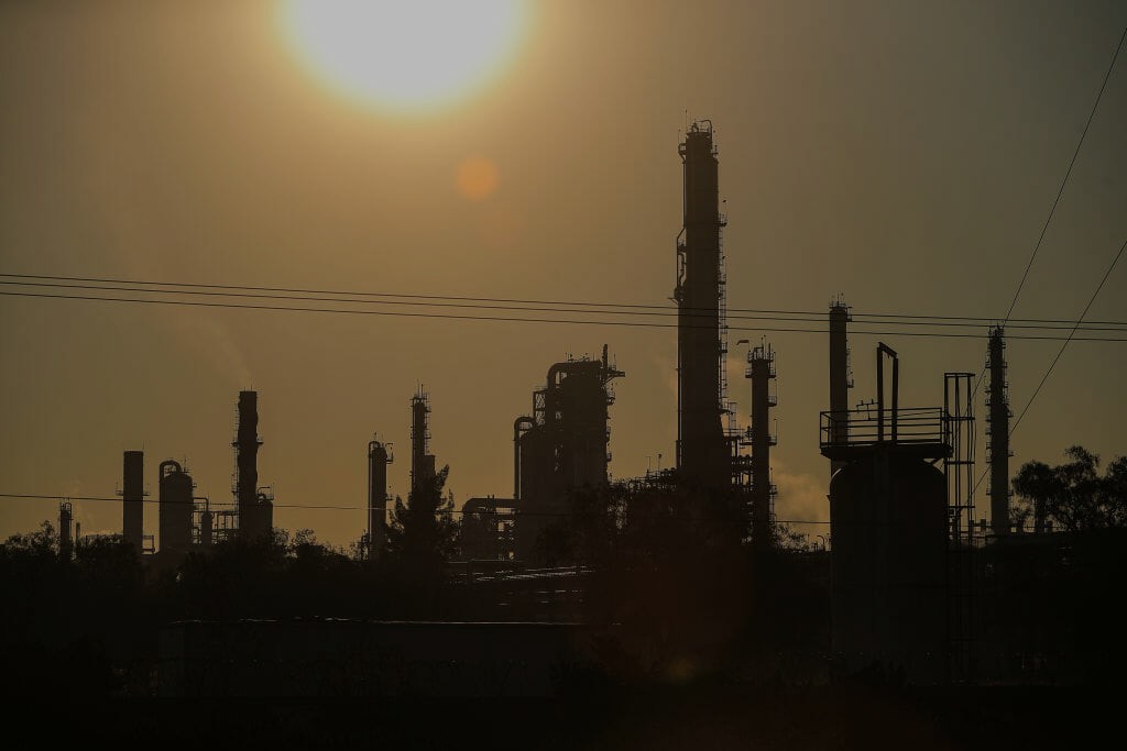 An sepia image of an oil refinery with the sun shining in the background