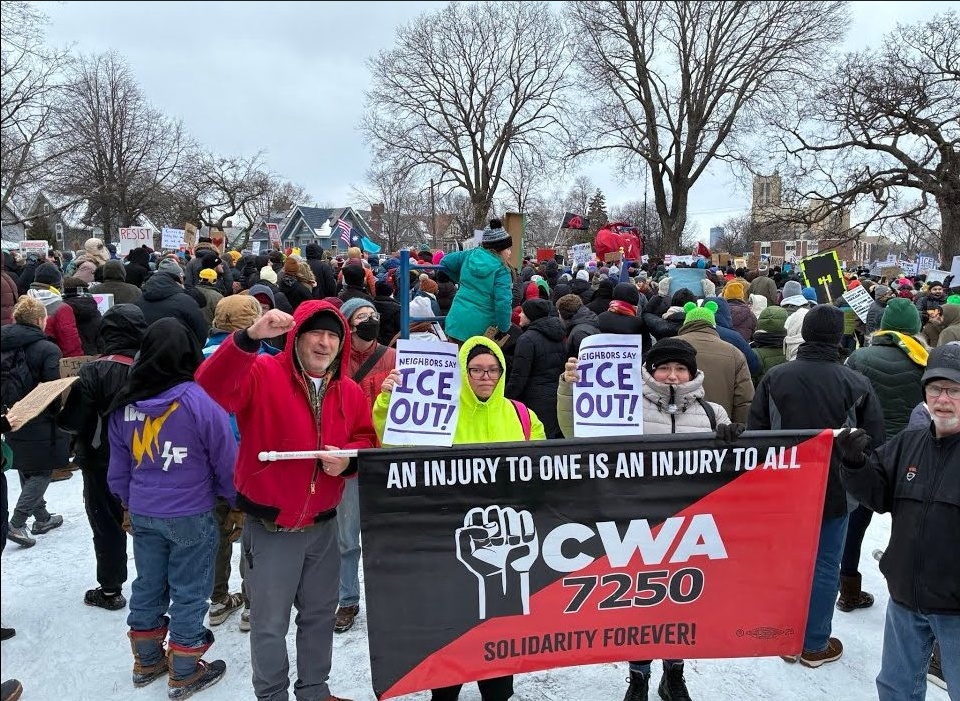 Photo of a group protesters standing in the snow with a banner reading "An injury to one is an injury to all"
