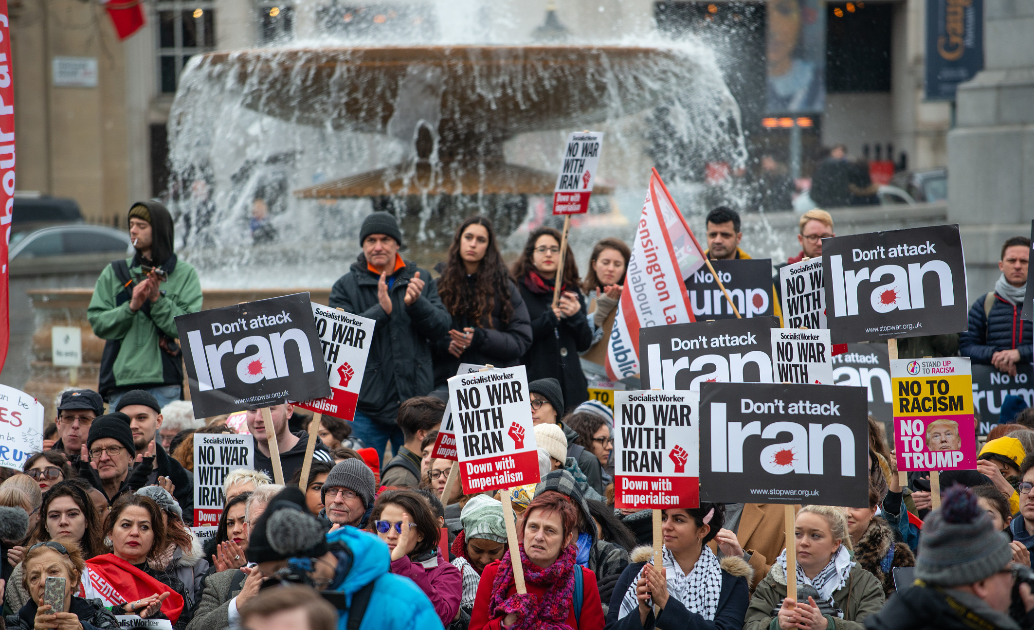 Photo of protesters holding various signs protesting a war with Iran.