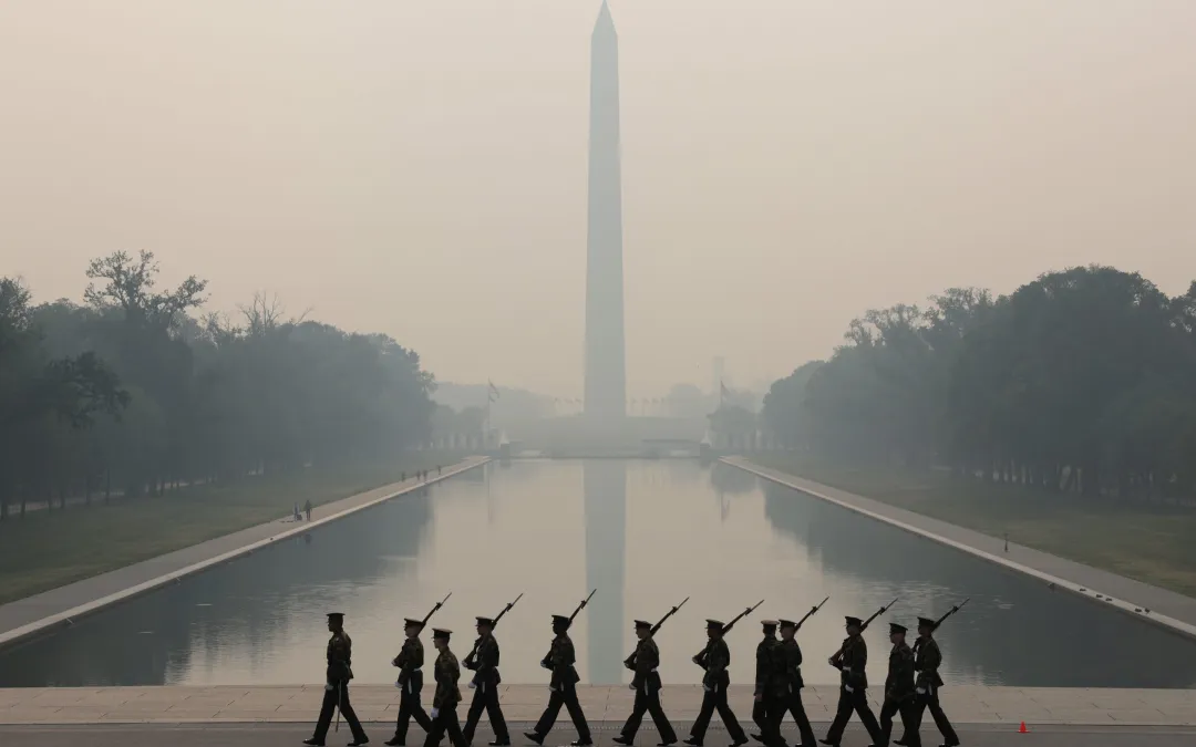 Photo of uniformed soldiers marching in front of the Reflecting Pool with the Washington Monument in the background.